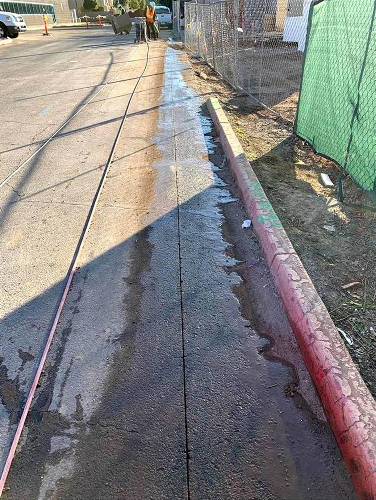 A long, straight saw cut through the pavement beside a curb, with the saw and operator working further up the line