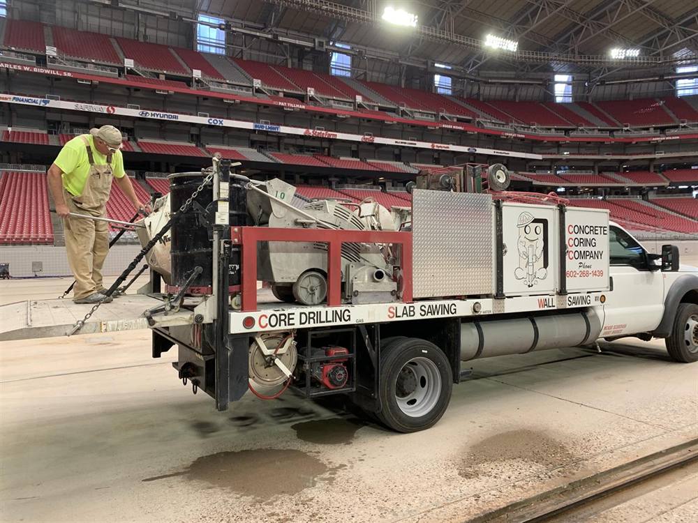 Concrete Coring Company truck 10 unloading a slab saw on the concrete floor of Cardinals Stadium in Glendale, Arizona, red seats behind
