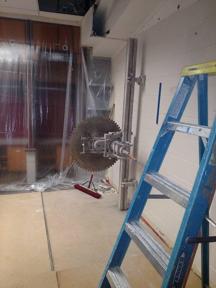 Track-mounted wall saw cutting an opening in a block wall inside Chase Field, the room sheeted off in plastic