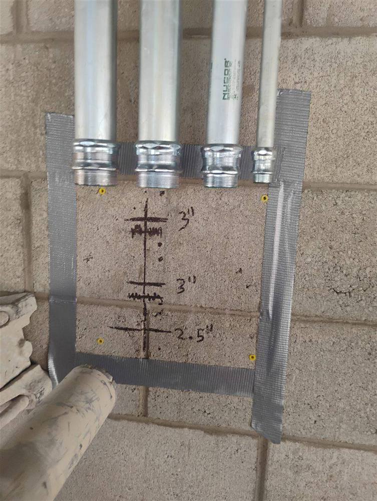 Block wall in Scottsdale with the core drilling layout marked under four conduit stub-ups: two 3-inch and one 2.5-inch