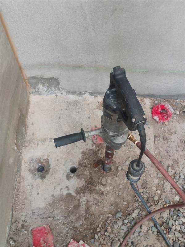 Hand-held wet core drill standing in a footer at Cosanti Commons in Scottsdale with two finished holes beside it